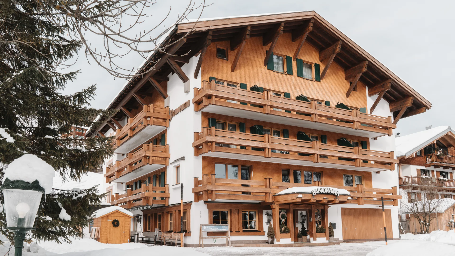 Verschneites Alpenhotel mit Holzbalkonen und grünen Fensterläden