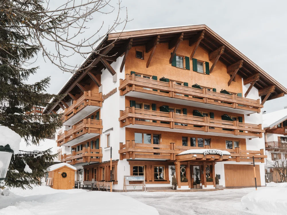 Ihre Auszeit in Lech am Arlberg Verschneites Alpenhotel mit Holzbalkonen und grünen Fensterläden