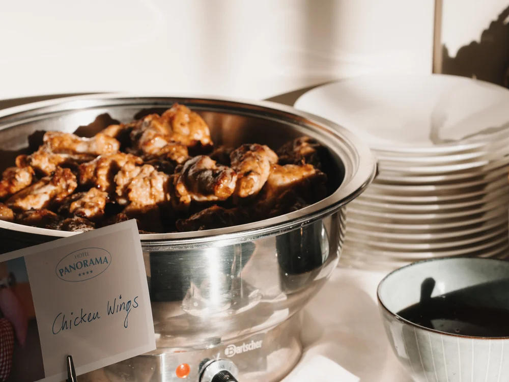 Ihre Auszeit in Lech am Arlberg Chicken Wings in einem Buffet-Warmhaltebehälter mit Tellern und Besteck