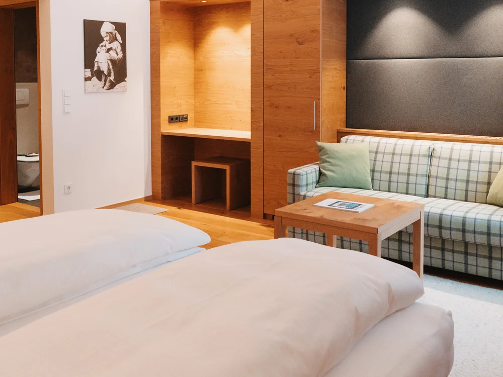 Ihre Auszeit in Lech am Arlberg Hotelzimmer mit großem Bett, kariertem Sofa und warmen Holzeinbauten