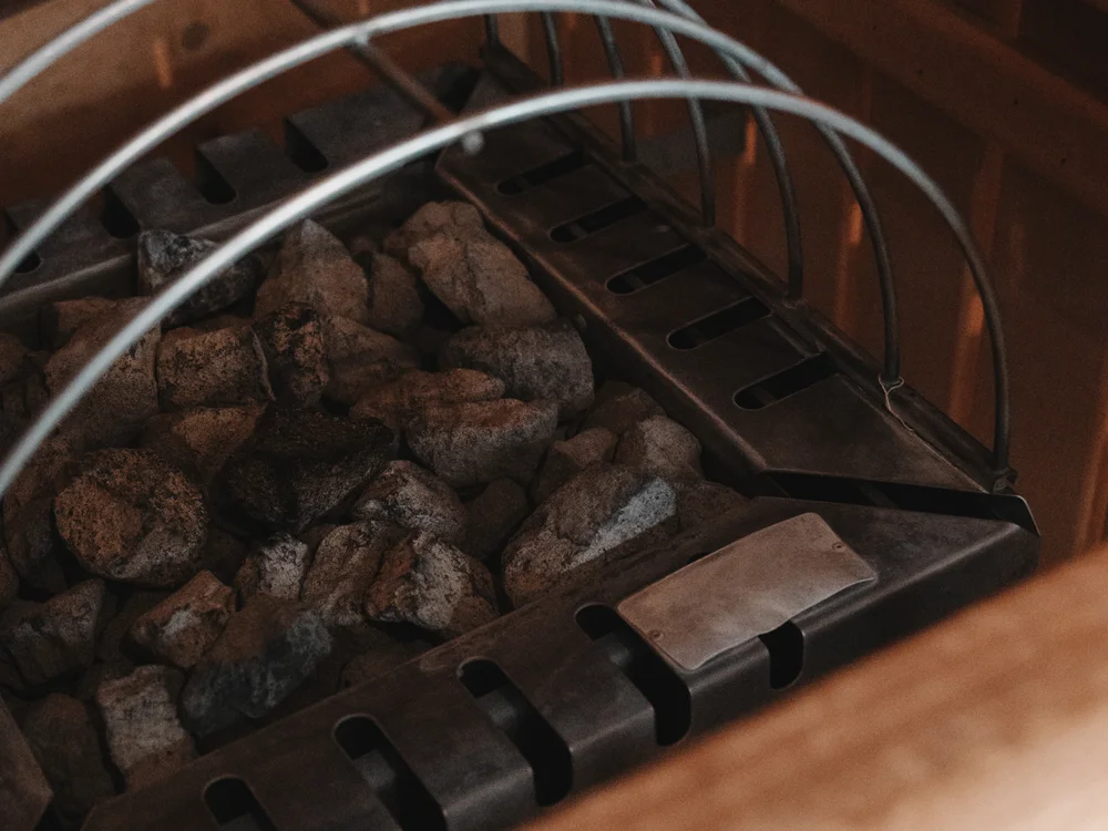 Ihre Auszeit in Lech am Arlberg Saunaofen mit Steinen und gebogenen Schutzbügeln aus Metall