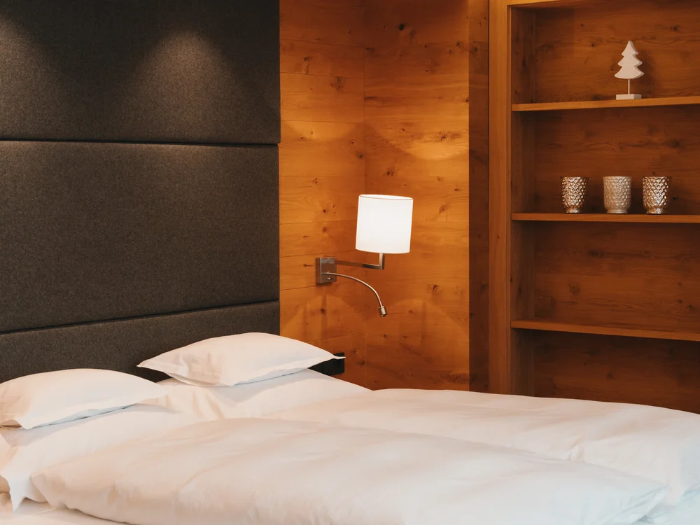 Ihre Auszeit in Lech am Arlberg Doppelbett mit weißer Bettwäsche in einem Schlafzimmer mit warmen Holzvertäfelungen