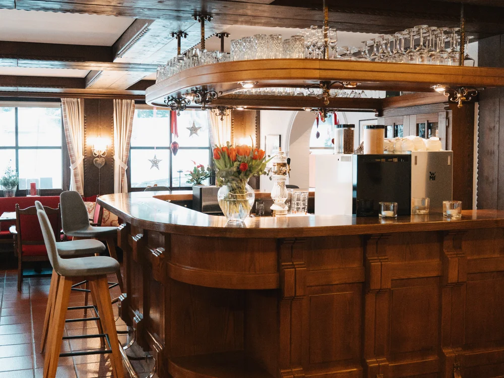 Ihre Auszeit in Lech am Arlberg Elegante Hotelbar aus Holz mit Gläsern, Blumen und Barhockern