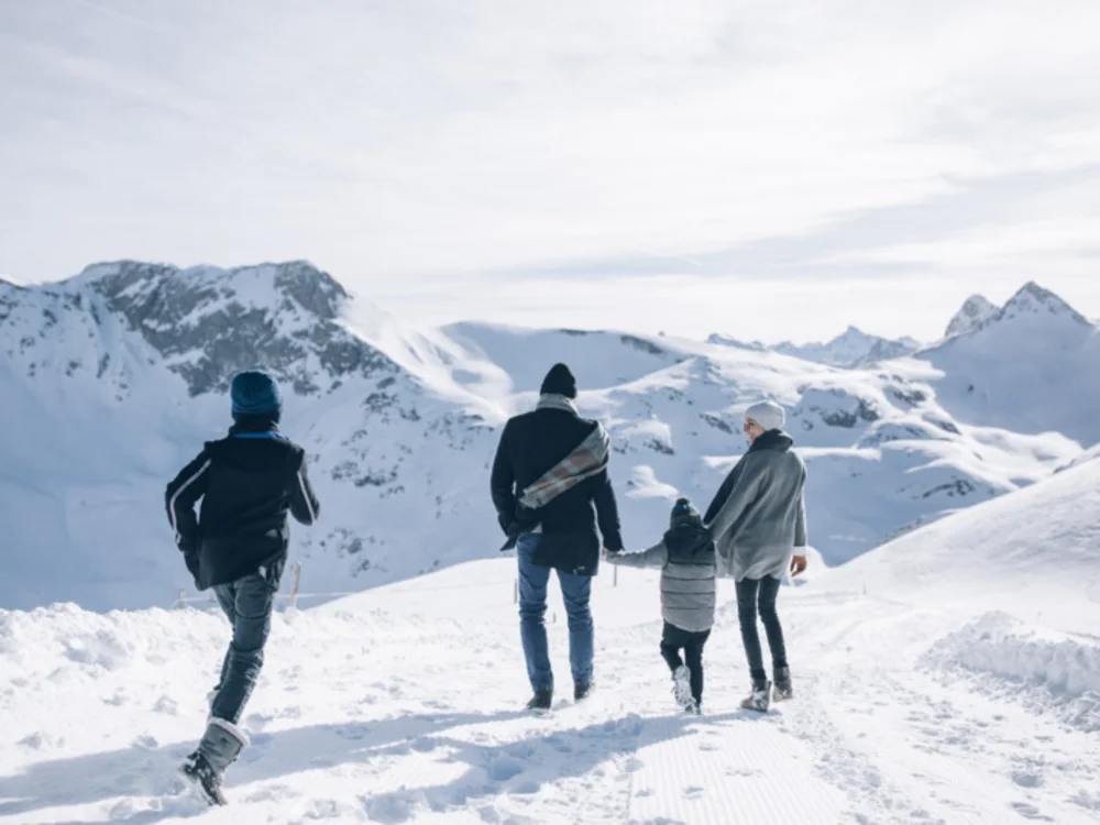 Ihre Auszeit in Lech am Arlberg Vier Personen gehen durch eine verschneite Berglandschaft