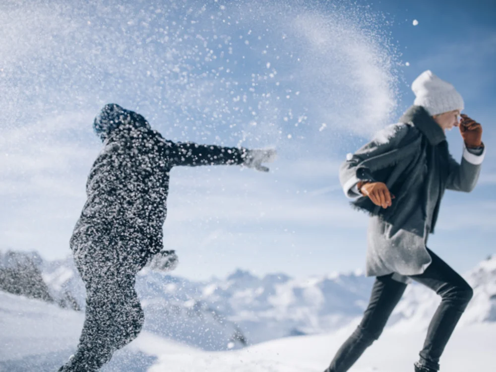 Two people playfully throw snow at each other in a snowy mountain landscape