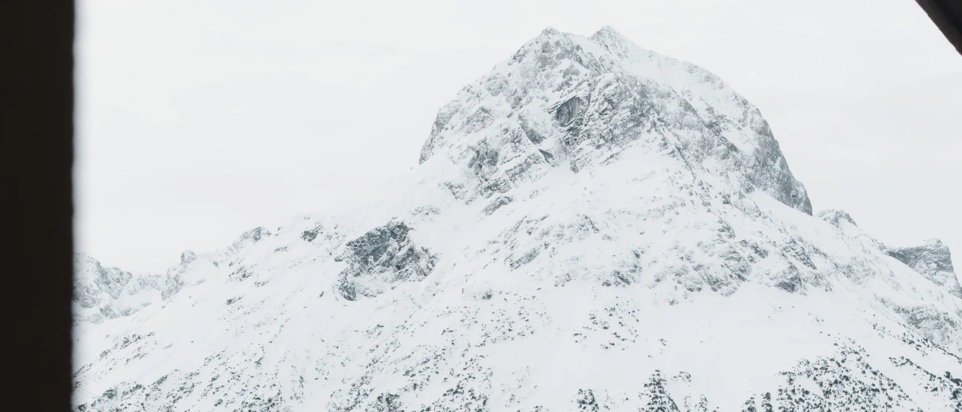 Snow-covered mountain village beneath a high snowy peak, framed by a window