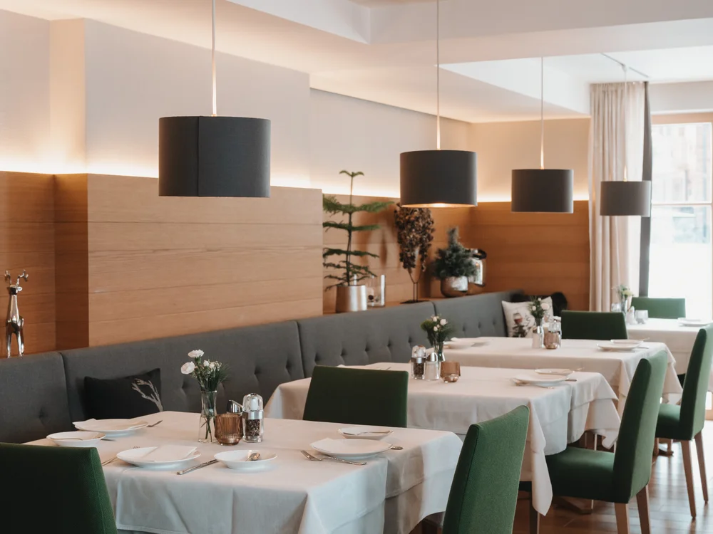 Ihre Auszeit in Lech am Arlberg Modernes Restaurant mit gedeckten Tischen, grünen Stühlen und schwarzen Pendelleuchten