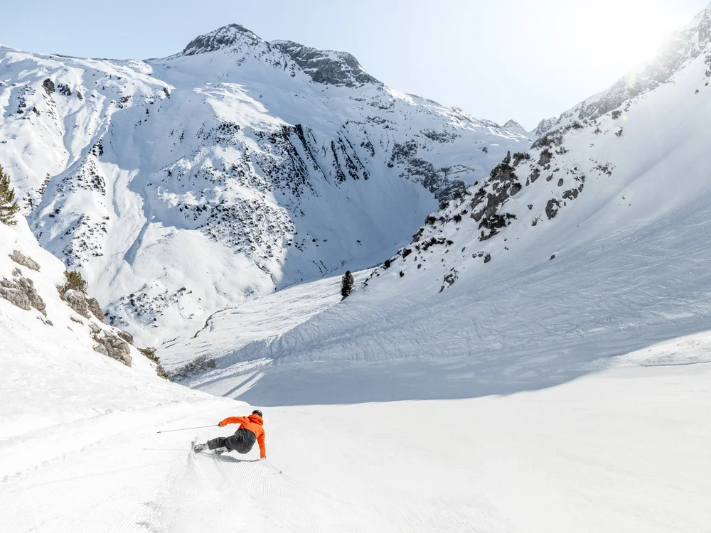Ihre Auszeit in Lech am Arlberg Skifahrer in orangefarbener Jacke fährt einen verschneiten Berghang hinunter