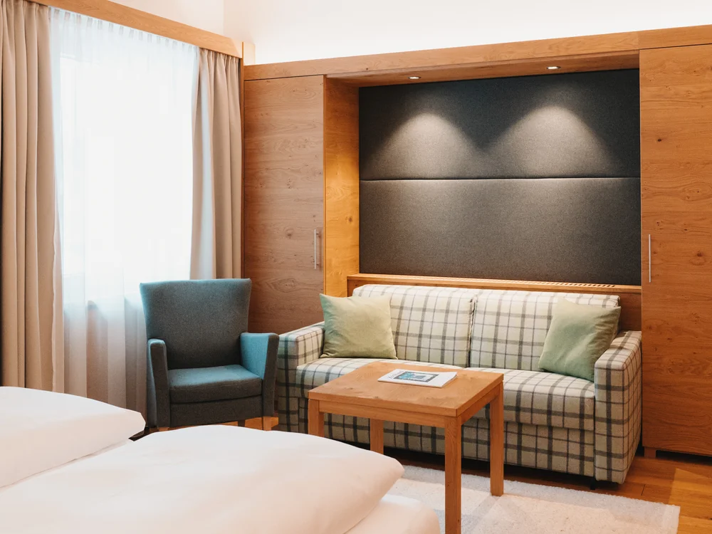 Ihre Auszeit in Lech am Arlberg Hotelzimmer mit Bett, kariertem Sofa, Sessel und kleinem Holztisch