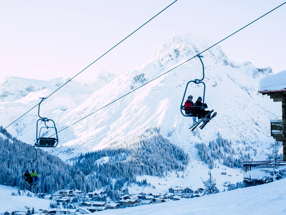 Skiers on chairlifts beneath a snow-covered mountain above a village