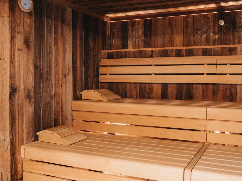 Ihre Auszeit in Lech am Arlberg Holzsauna mit mehrstufigen Sitzbänken und Uhr an der Wand
