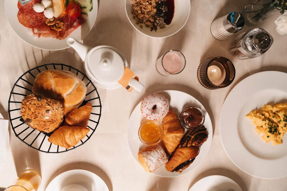 Frühstückstisch mit Brot, Gebäck, Aufschnitt, Joghurt und Beilagen