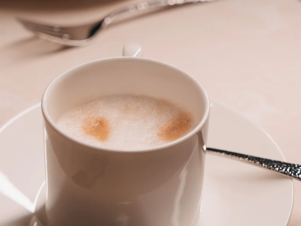 Ihre Auszeit in Lech am Arlberg Weiße Kaffeetasse mit Milchschaum auf Untertasse und Besteck