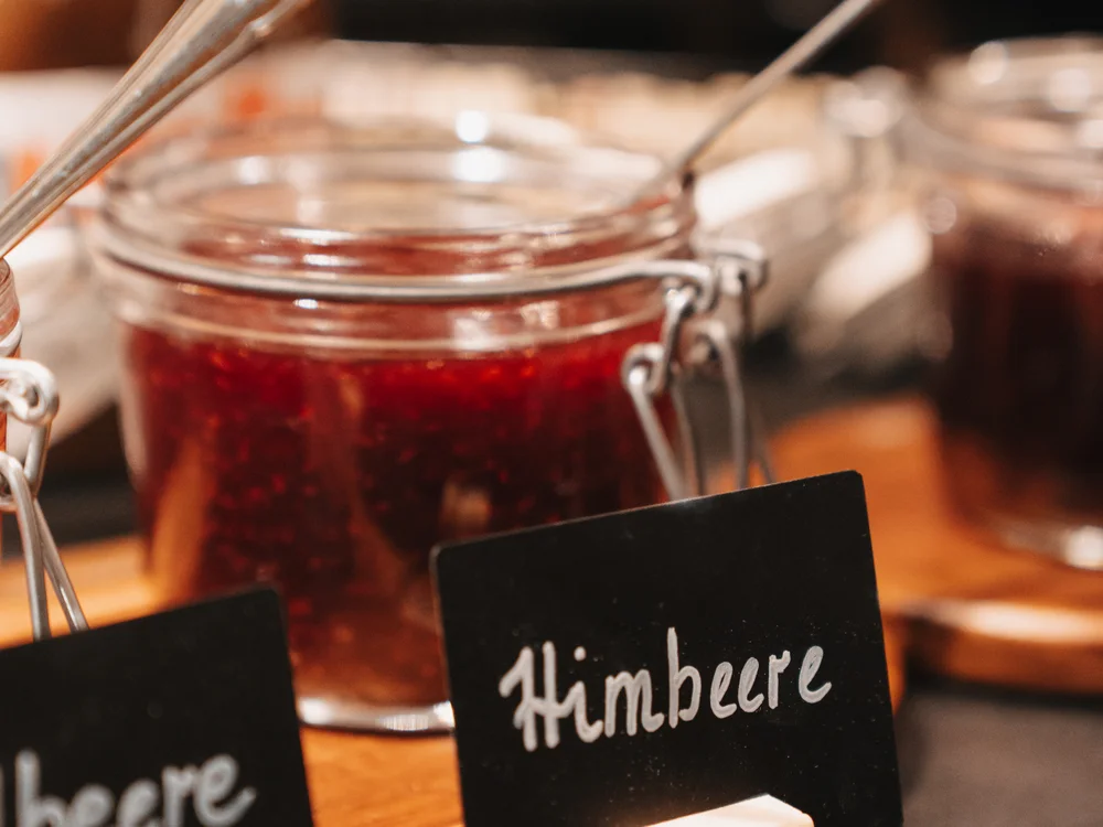 Ihre Auszeit in Lech am Arlberg Glas mit roter Himbeerkonfitüre und schwarzem Schild mit der Aufschrift Himbeere