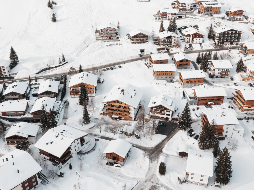 Ihre Auszeit in Lech am Arlberg Luftaufnahme eines verschneiten Bergdorfs mit Häusern, Straßen und Tannenbäumen
