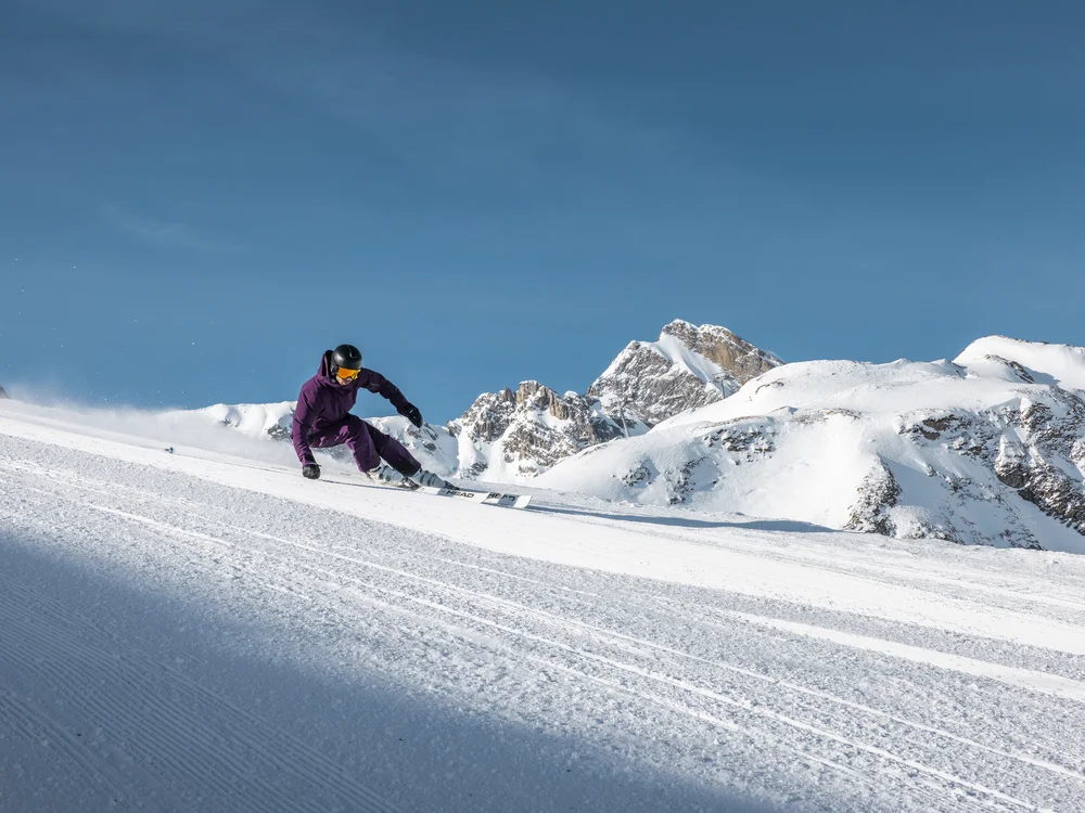 Ihre Auszeit in Lech am Arlberg Skifahrer fährt auf einer präparierten Piste vor schneebedeckten Bergen