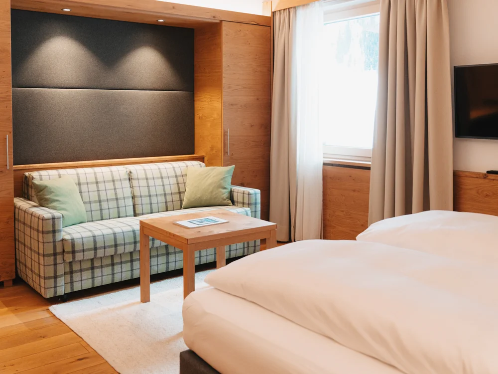 Ihre Auszeit in Lech am Arlberg Hotelzimmer mit großem Bett, kariertem Sofa, Holztisch und Fernseher