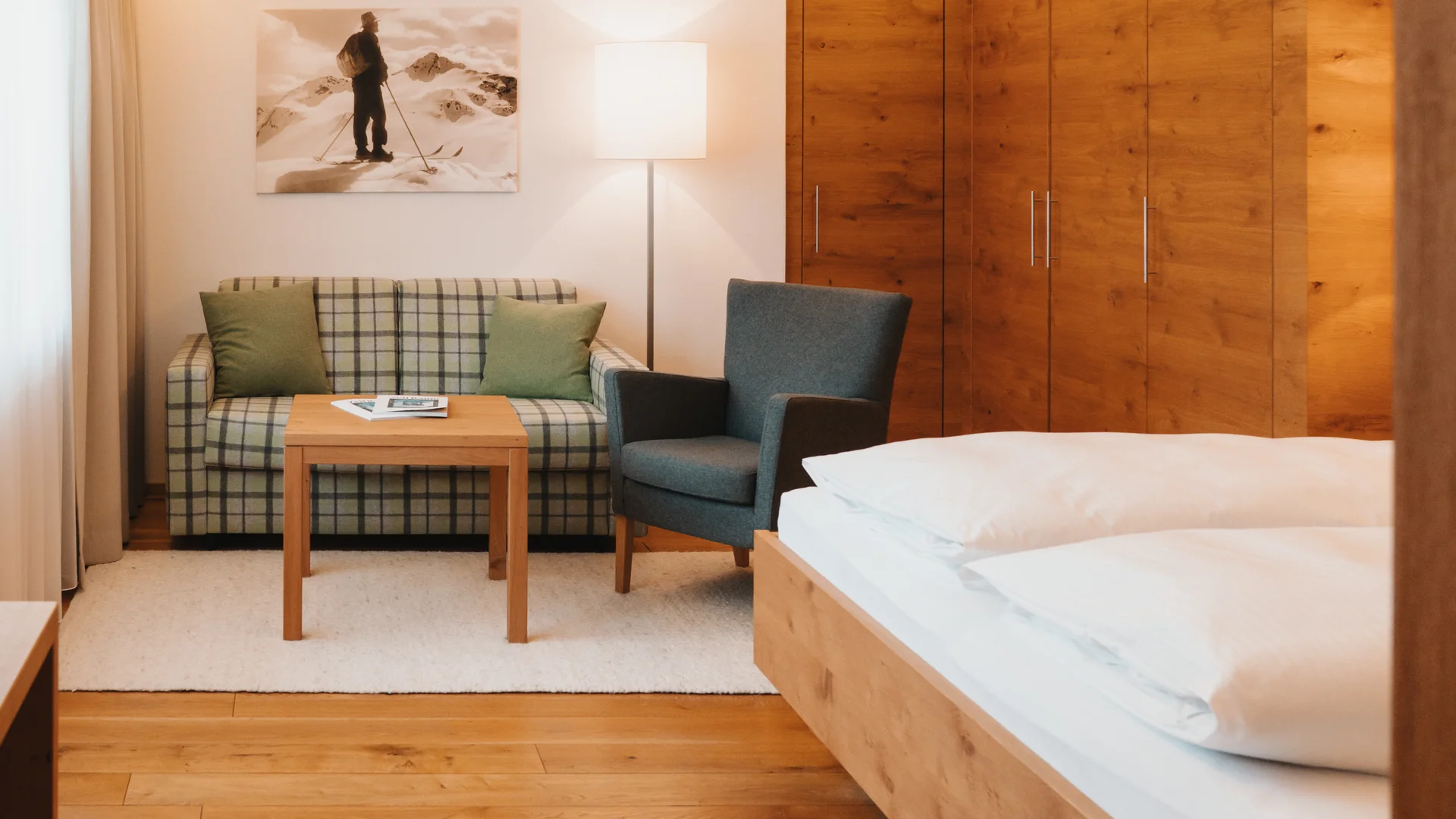 Hotelzimmer mit Holzbett, Einbauschrank, Sofa und Sessel