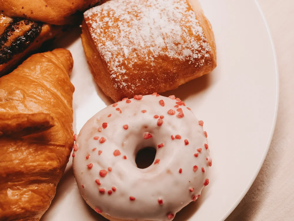 Ihre Auszeit in Lech am Arlberg Teller mit Croissants, süßem Gebäck und einem glasierten Donut mit roten Streuseln