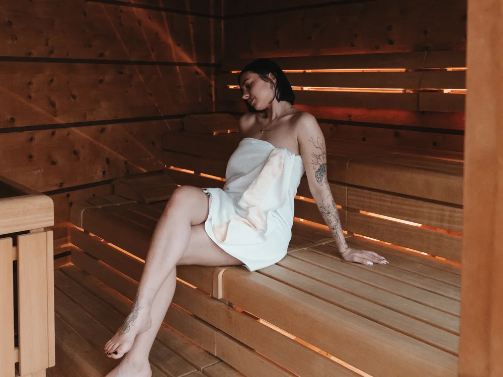 Ihre Auszeit in Lech am Arlberg Frau im weißen Handtuch entspannt auf den Holzbänken einer Sauna