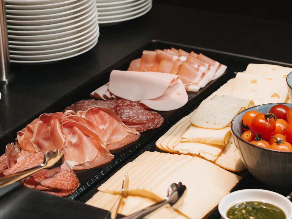 Ihre Auszeit in Lech am Arlberg Frühstücksbuffet mit Aufschnitt, Käse, Tomaten und gestapelten Tellern