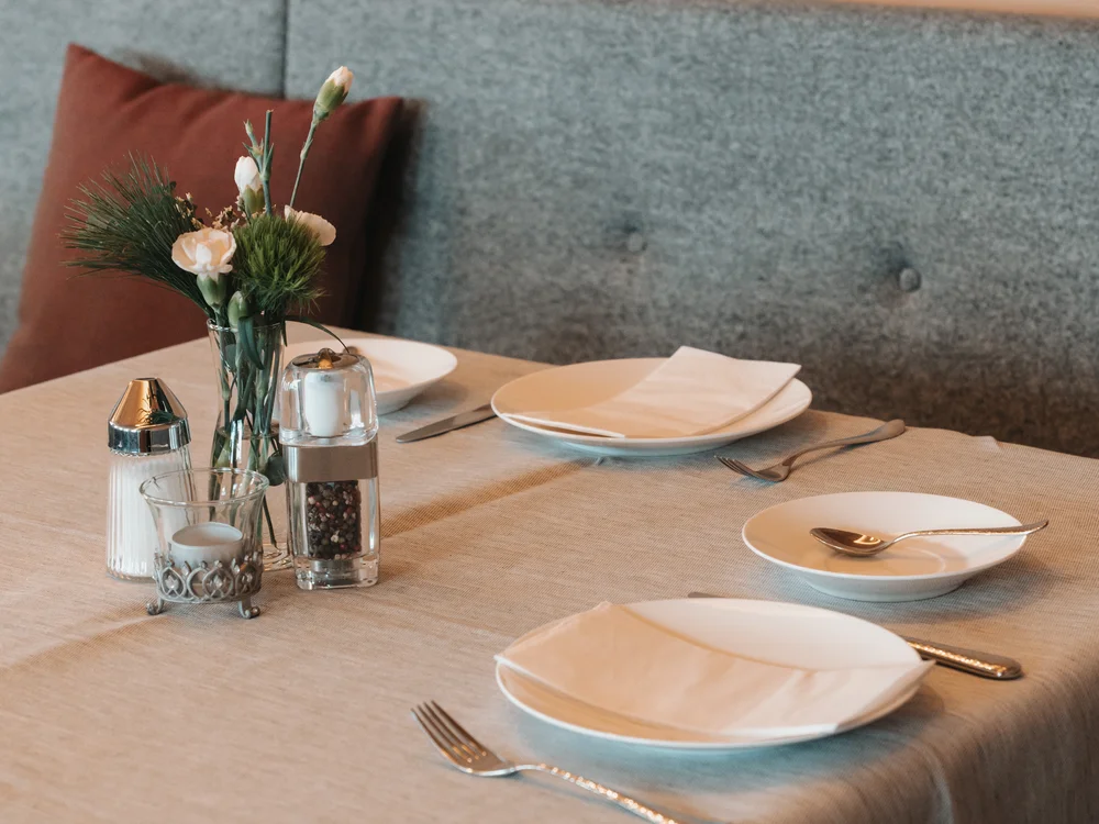 Ihre Auszeit in Lech am Arlberg Gedeckter Restauranttisch mit Tellern, Besteck und Blumenvase vor Holzverkleidung