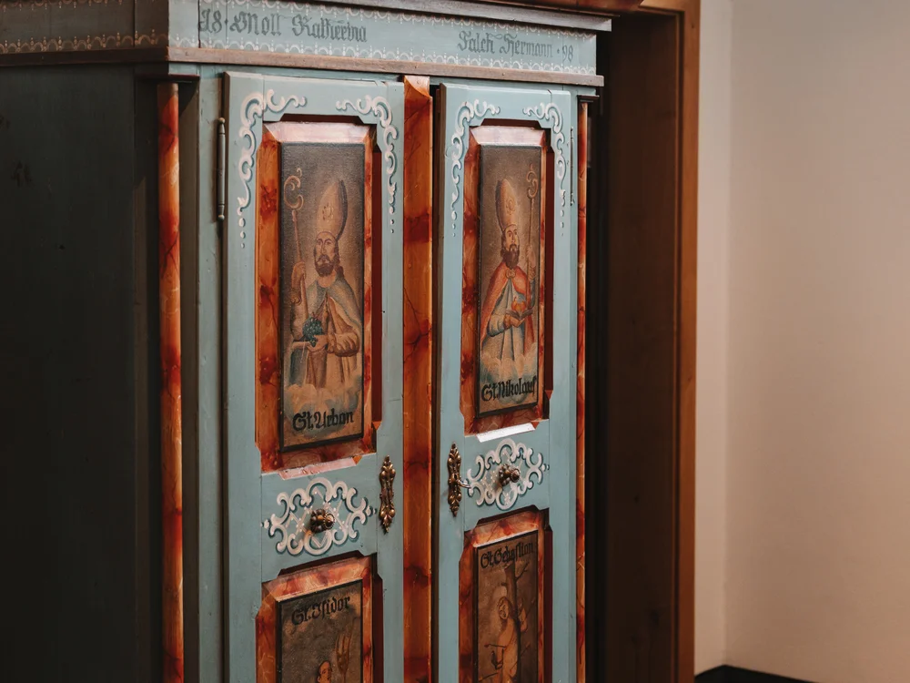 Ihre Auszeit in Lech am Arlberg Verzierter blau-roter Holzschrank mit gemalten Figuren auf den Türen
