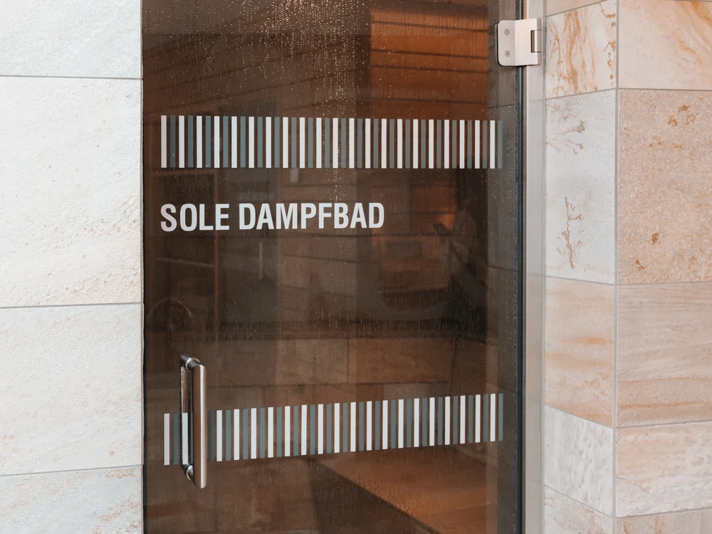 Glass door to the salt steam bath in a light-tiled spa area