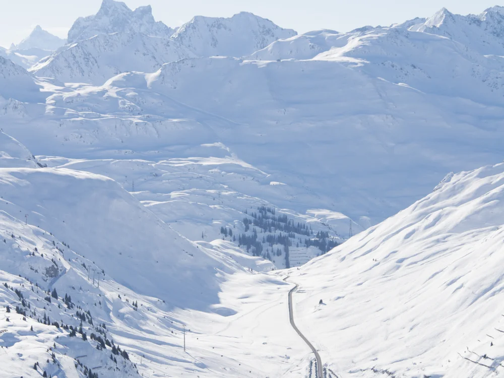 Ihre Auszeit in Lech am Arlberg Verschneites Alpental mit Bergdorf, kurvenreicher Straße und schneebedeckten Gipfeln