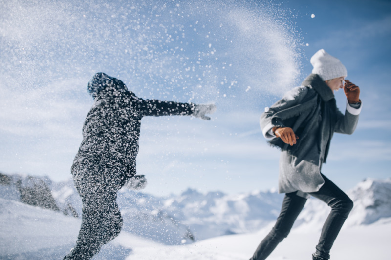 Ihre Auszeit in Lech am Arlberg Zwei Menschen werfen sich lachend Schnee zu, umgeben von einer verschneiten Berglandschaft